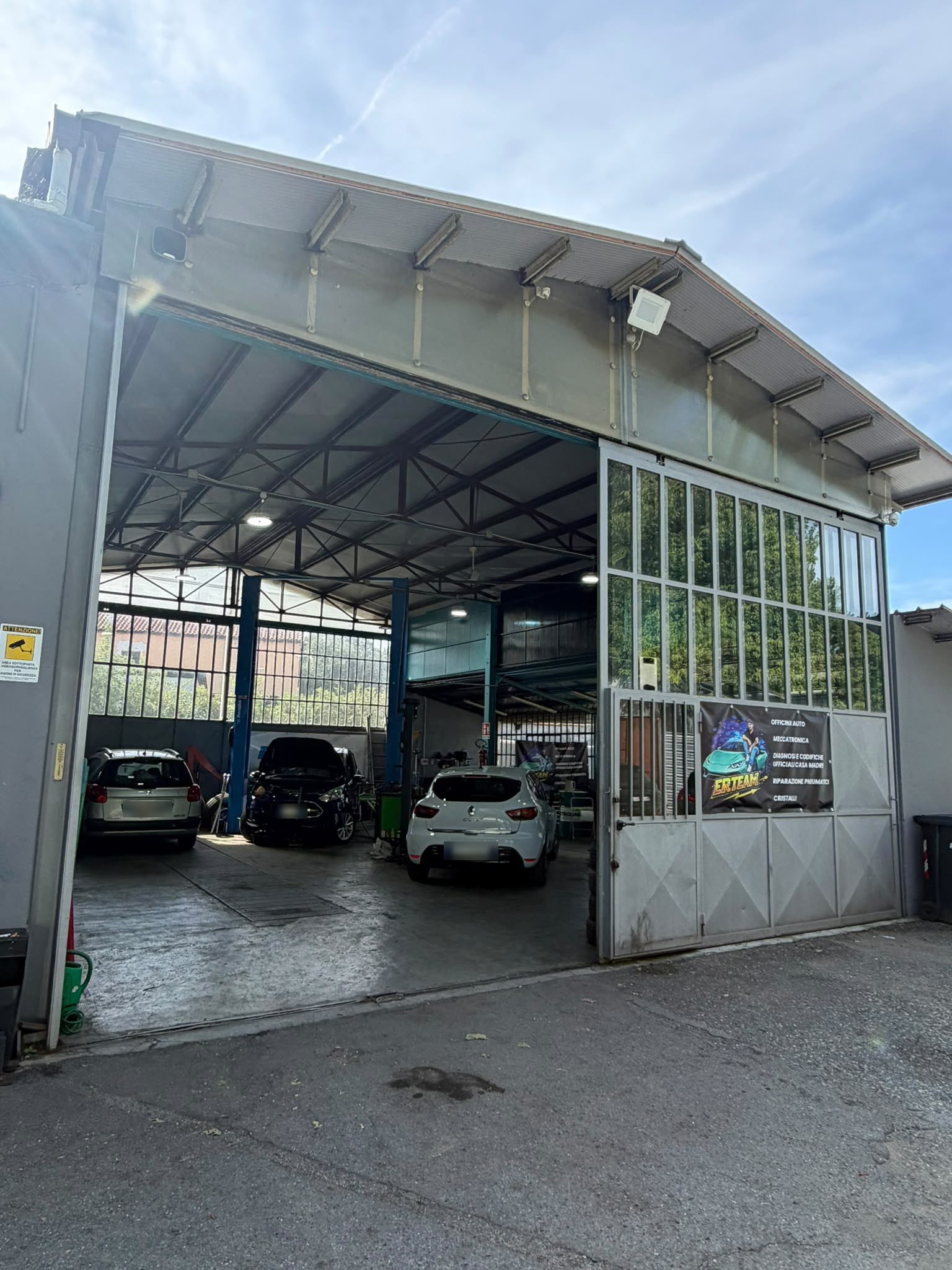 Capannone di E.R.TEAM con il portone aperto, auto in lavorazione sui ponti e lo striscione dei servizi